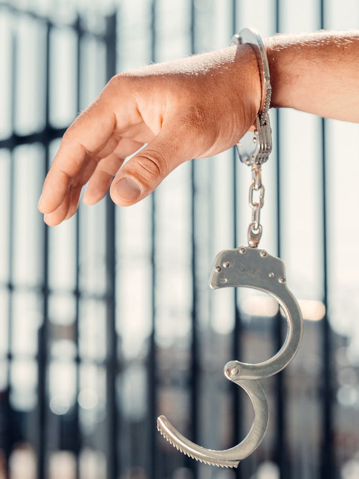 pexels-photo-7785079 A close-up, conceptual shot of a handcuffed hand with one open handcuff against blurred bars.