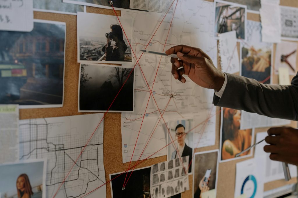 pexels-photo-8369520-8369520 Detective examines a corkboard with maps and photos to solve a mystery.